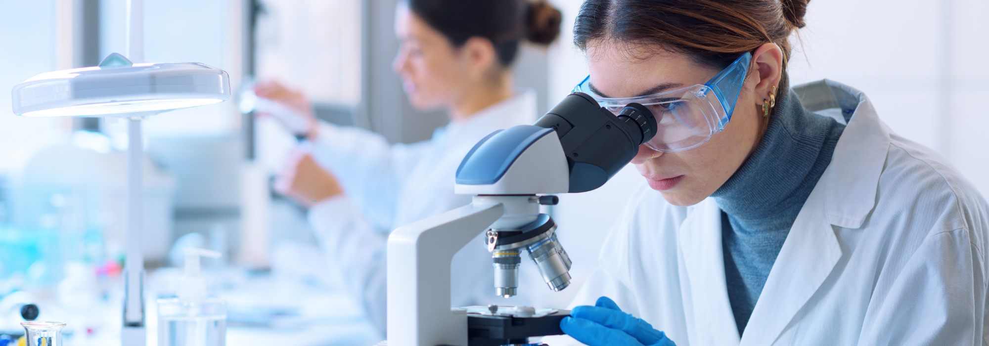 Female scientist using a microscope in a laboratory, representing clinical trial security and the protection of sensitive patient data in life sciences research