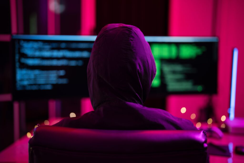 Hacker in dark hoodie facing multiple screens with stolen data, symbolizing compromised credentials and cybersecurity breaches in healthcare and enterprise environments